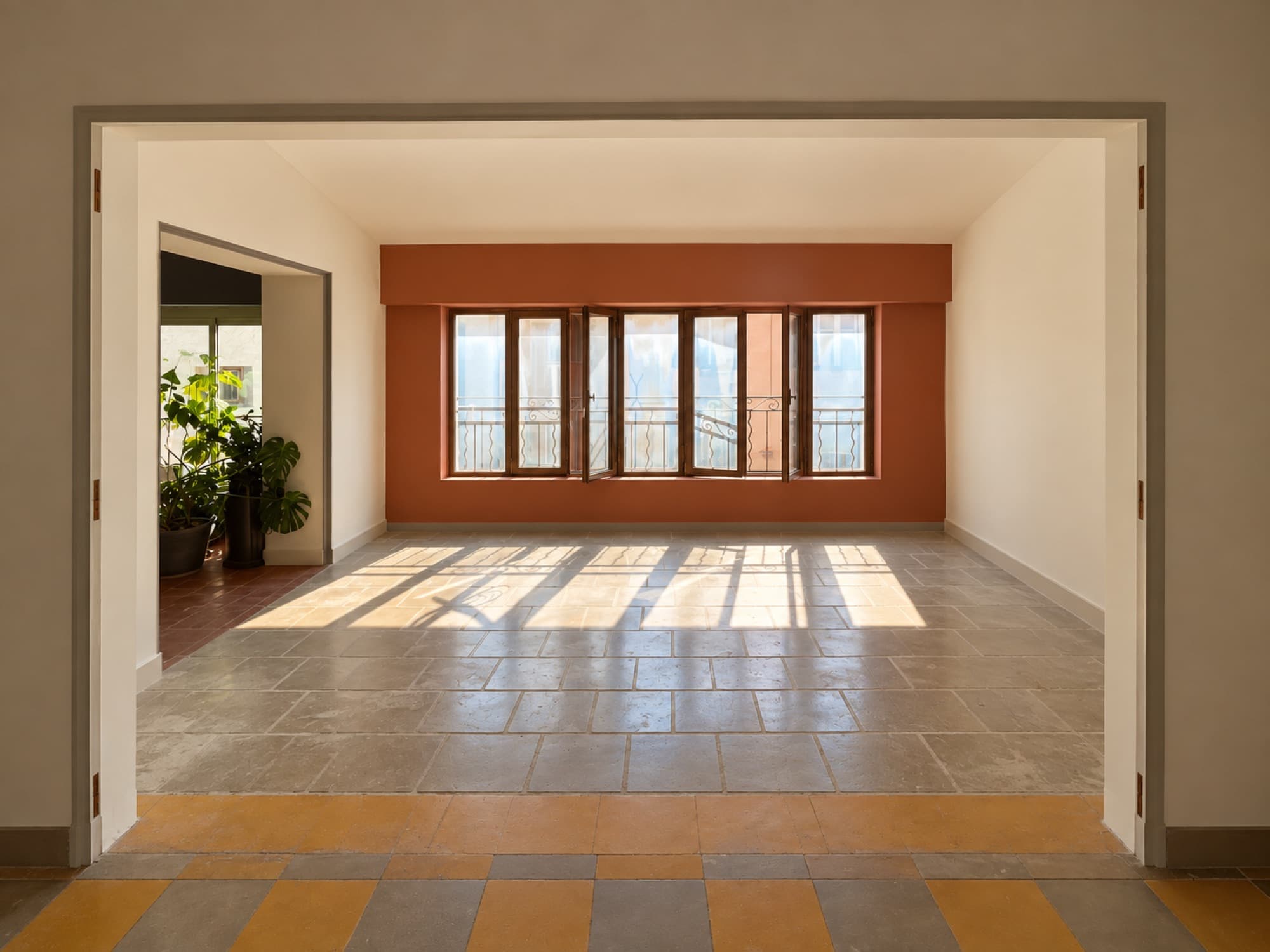 Séjour rénové : mur terracotta, fenêtres en enfilade et sol en pierre baigné de soleil