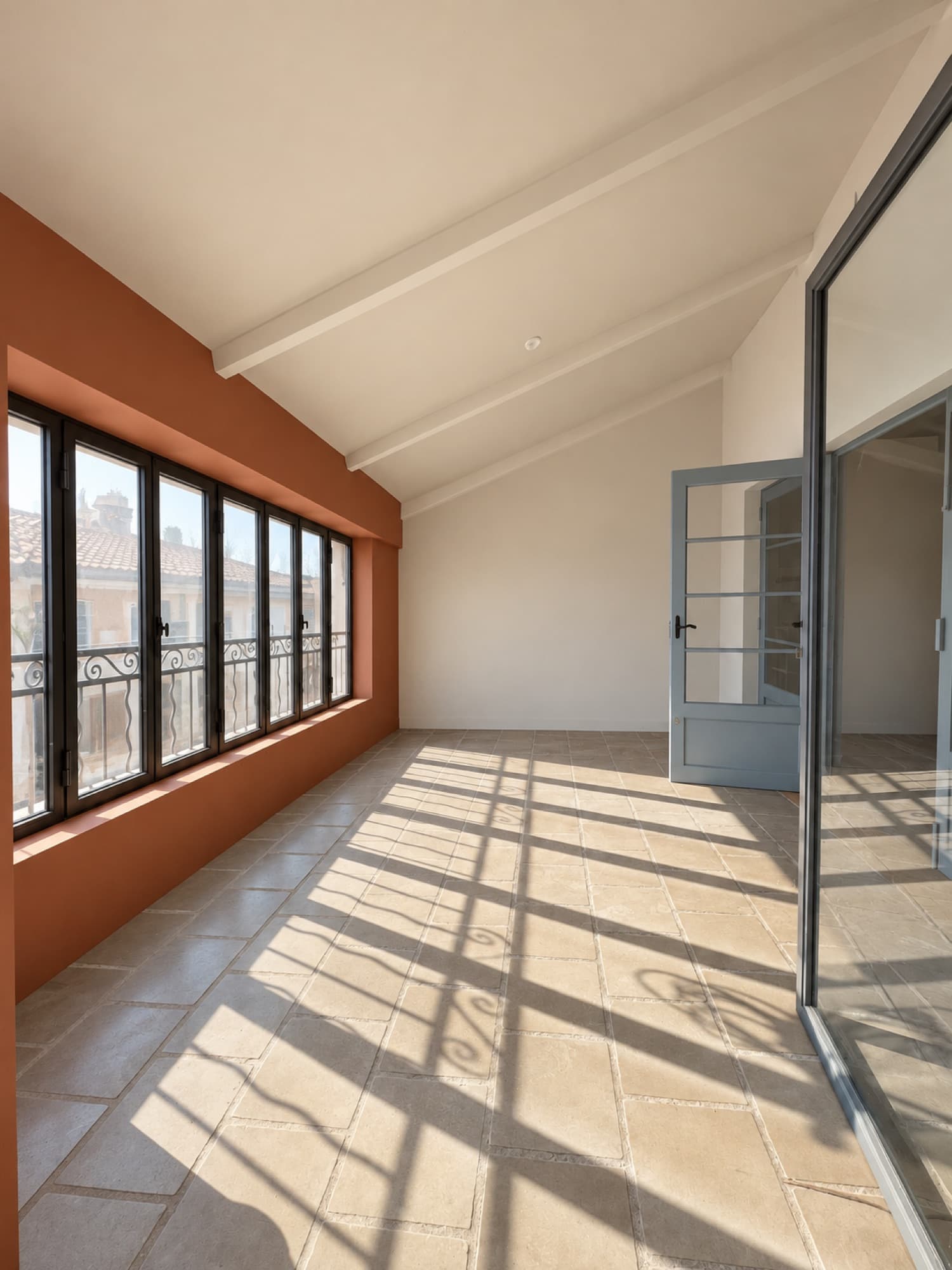 Pièce lumineuse aux fenêtres en enfilade, mur terracotta et porte vitrée bleue
